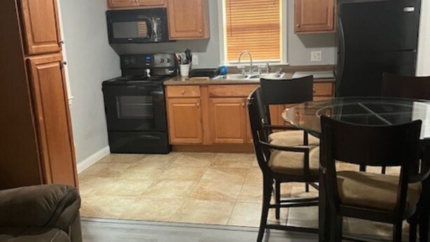 A compact kitchen with wooden cabinets, a black refrigerator, and a dining area with a glass table and chairs.