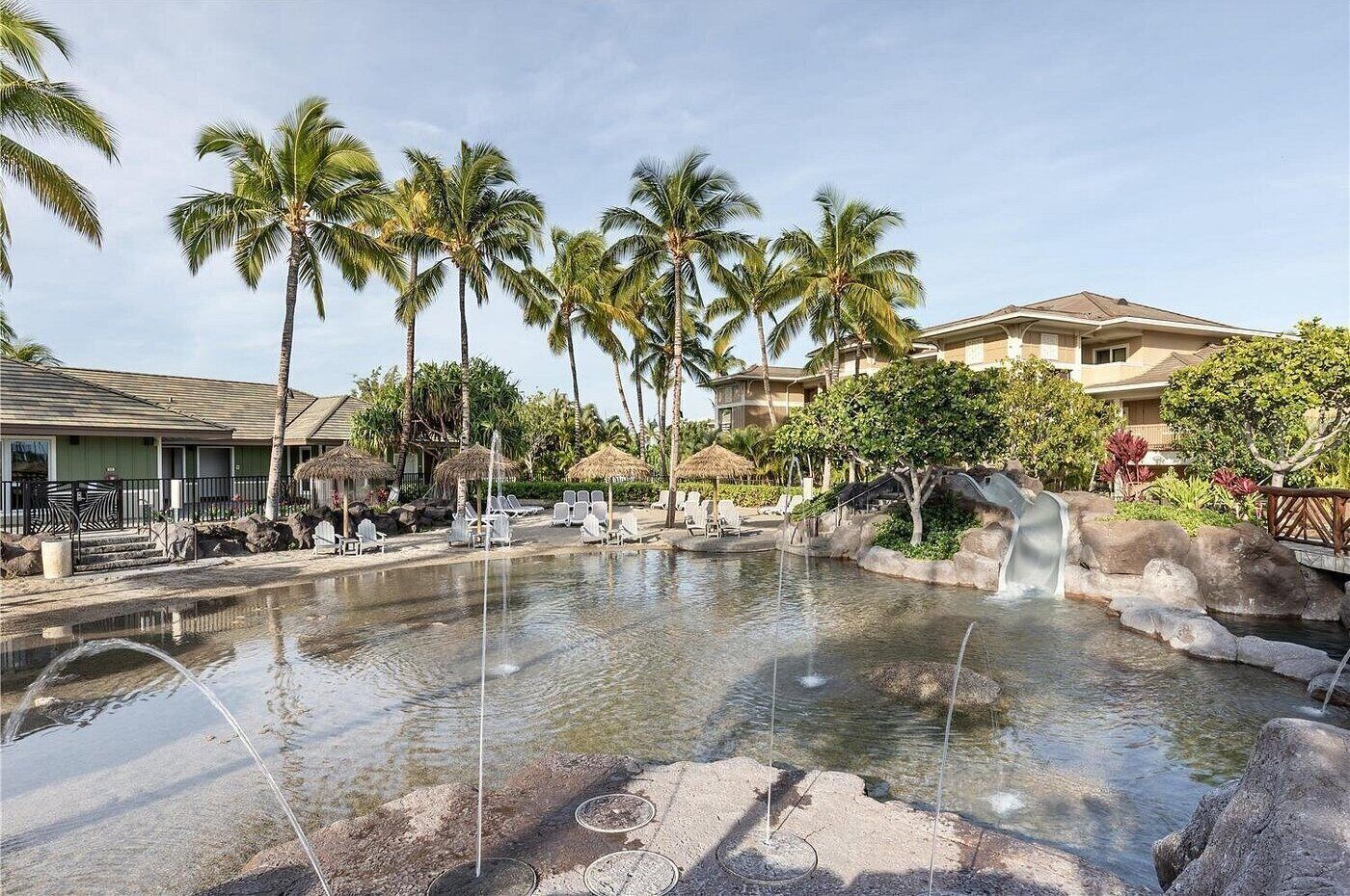 Pool på resort med palmer, liggestole og et vandfald.