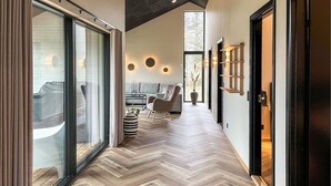 Een modern interieur met een visgraatparketvloer, een bank, een fauteuil en een groot raam met zonwering.
