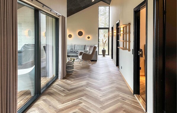 A modern interior with a herringbone wooden floor, a sofa, a chair, and a large window with blinds.