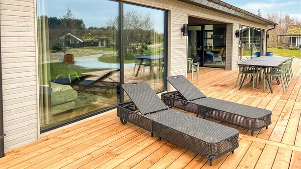 Een modern huis met grote schuifdeuren, een houten terras en tuinmeubilair.