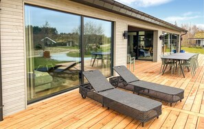A modern house with large sliding glass doors, a wooden deck, and outdoor furniture.