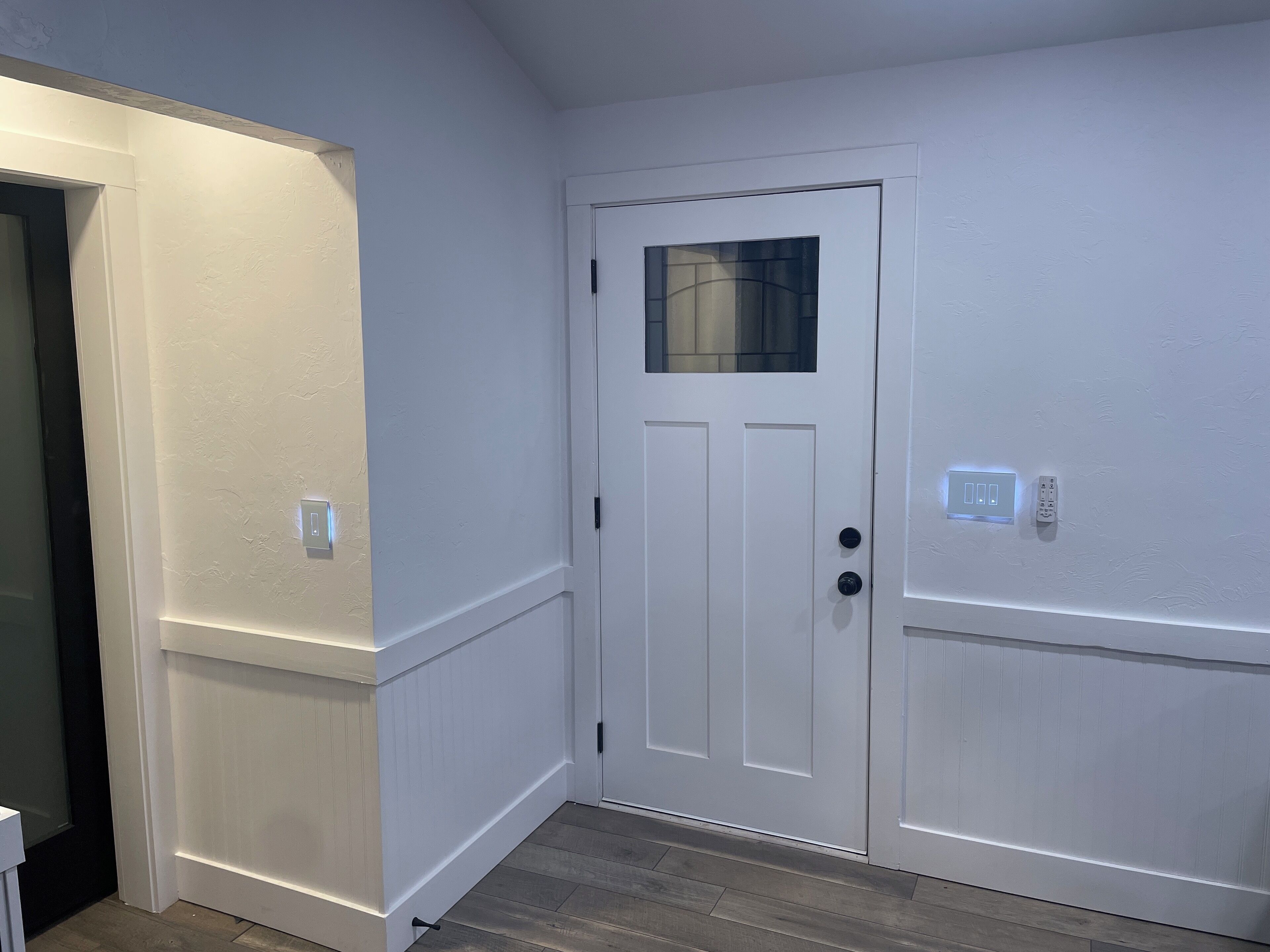 A white door with a small window, a light switch, and a power outlet on the wall.