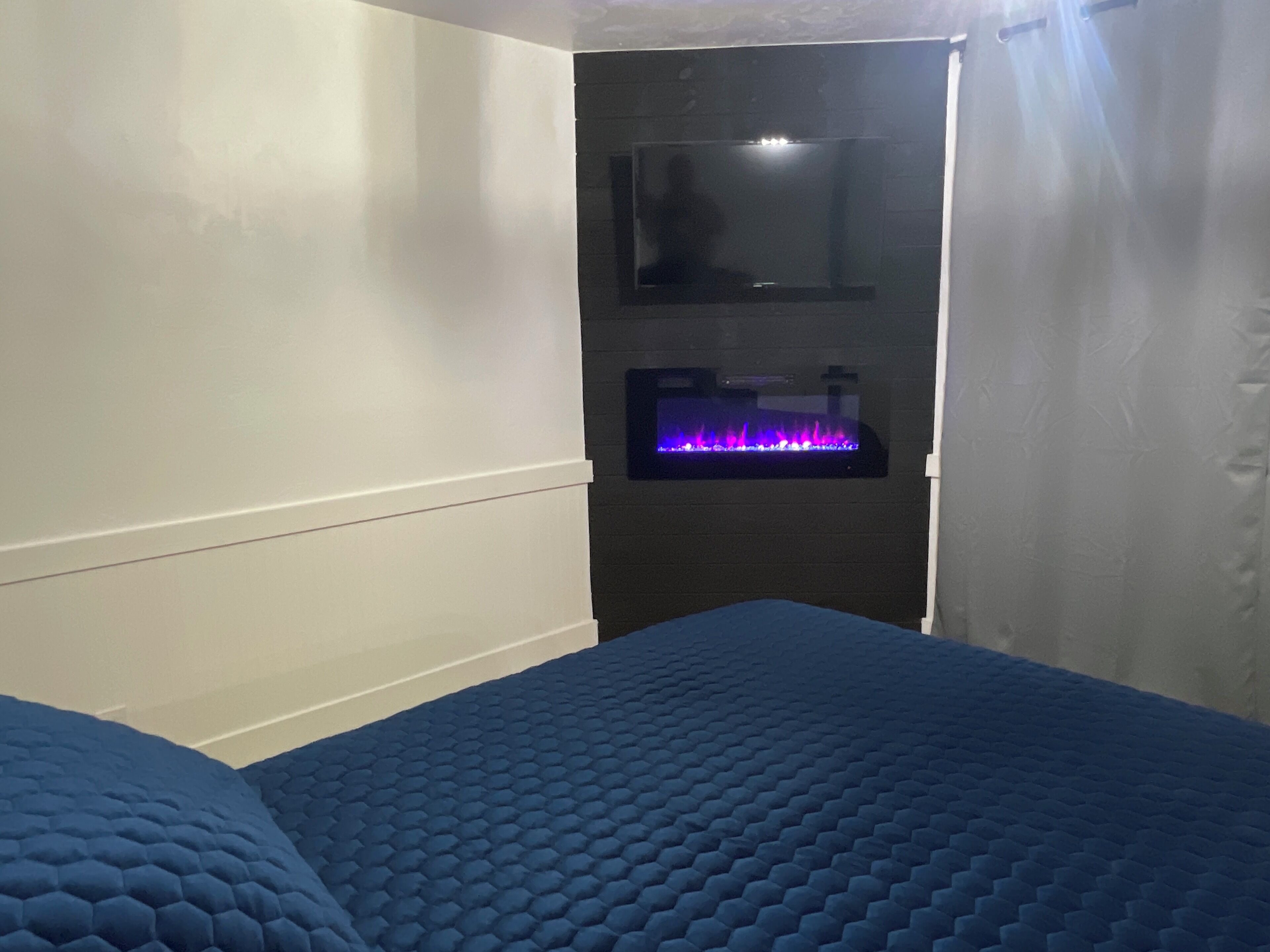 Une chambre à coucher avec une couvre-lit bleue à motifs, une étagère fixée au mur avec un éclairage bleu, et un miroir.
