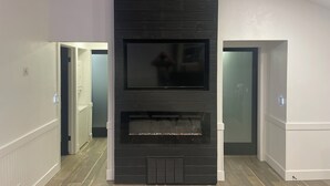 A modern living room with a large black entertainment unit, a fireplace, and a flat-screen TV. - Charming 2-bedroom house with AC and WiFi in lovely Wanette (Wanette)