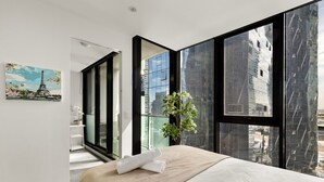 A modern hotel room with a large bed, a view of the city through floor-to-ceiling windows, and a painting of the Eiffel Tower.