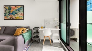 A modern living room with a grey sofa, a white desk, and a colorful abstract painting.