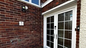 Fachada de ladrillo con una puerta blanca, un banco y un letrero que indica la dirección.