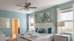 Un dormitorio con cama, mesitas de noche, ventilador de techo, ventana y puerta.