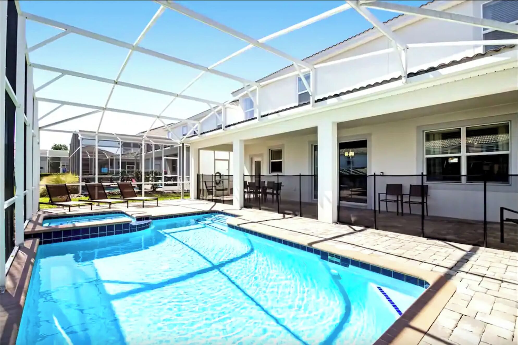 A swimming pool with a glass enclosure, outdoor seating, and a covered patio area.