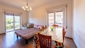Ein geräumiges Zimmer mit großem Esstisch, Holzstühlen, einer Couch und einer bettenausgestatteten Bettdecke mit Muster.