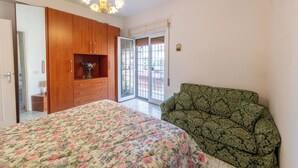 Ein Schlafzimmer mit Bett, einem grün gemusterten Sofa, einem Holzschrank und einer Kristallleuchter.