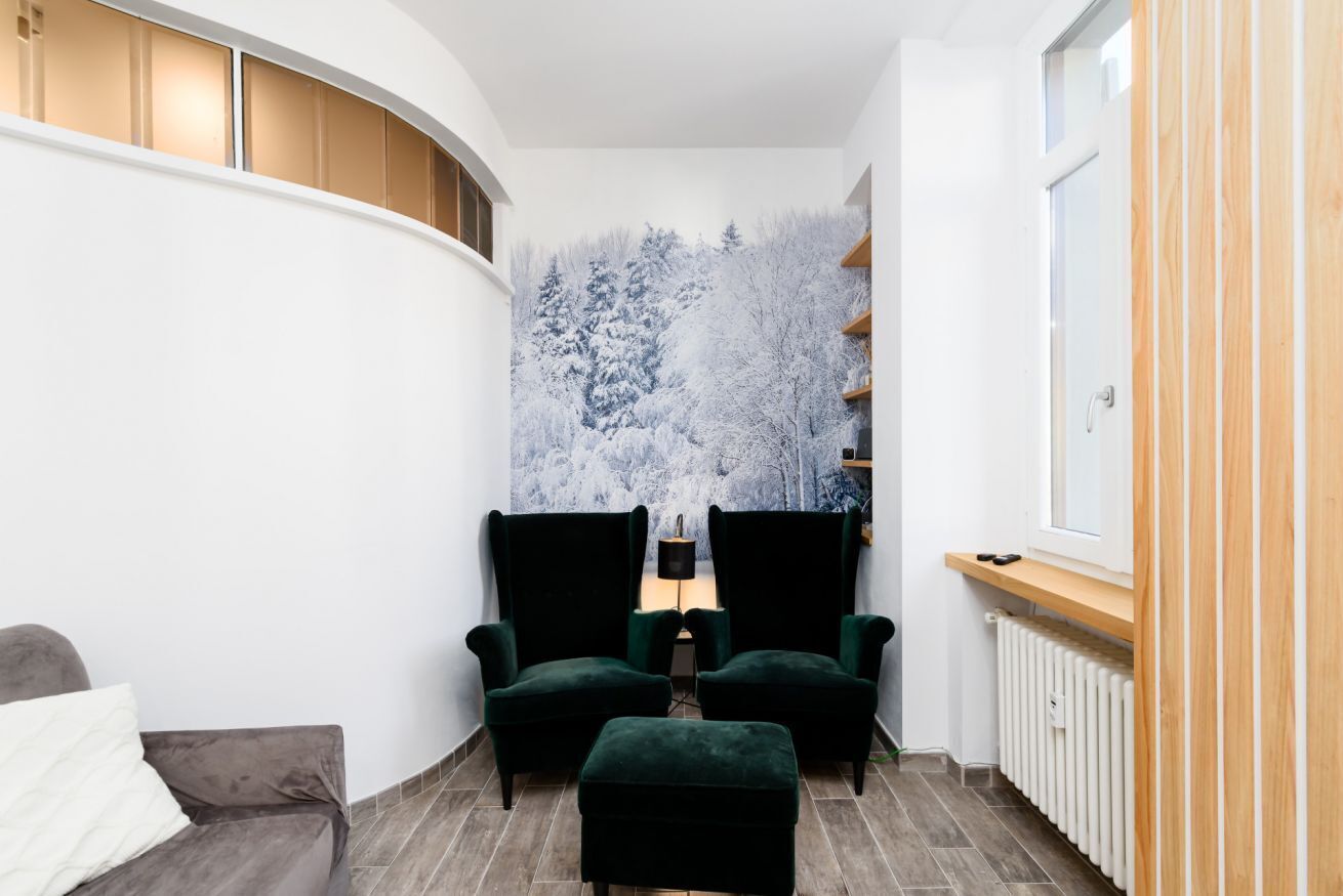 A modern room with a curved white wall, a large window, a radiator, and a green upholstered chair.