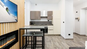 A modern kitchen with a dining area, a fireplace, and a large flat-screen TV mounted on the wall.