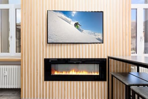 A modern interior with a fireplace, a television mounted on a wooden wall, and a window with a view of the outdoors.