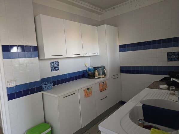 A kitchen with white cabinets, blue and white tiles, a green trash bin, and a sink with a faucet.