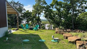 A backyard with a covered patio, green chairs, and a view of a lake. - Large porch offers beautiful views of the lake. Enjoy unique interior design! (Mannford)