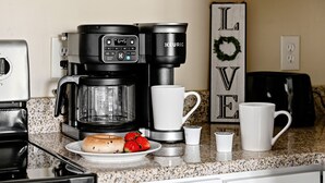 Una cocina con una cafetera, un plato de fresas y una taza.