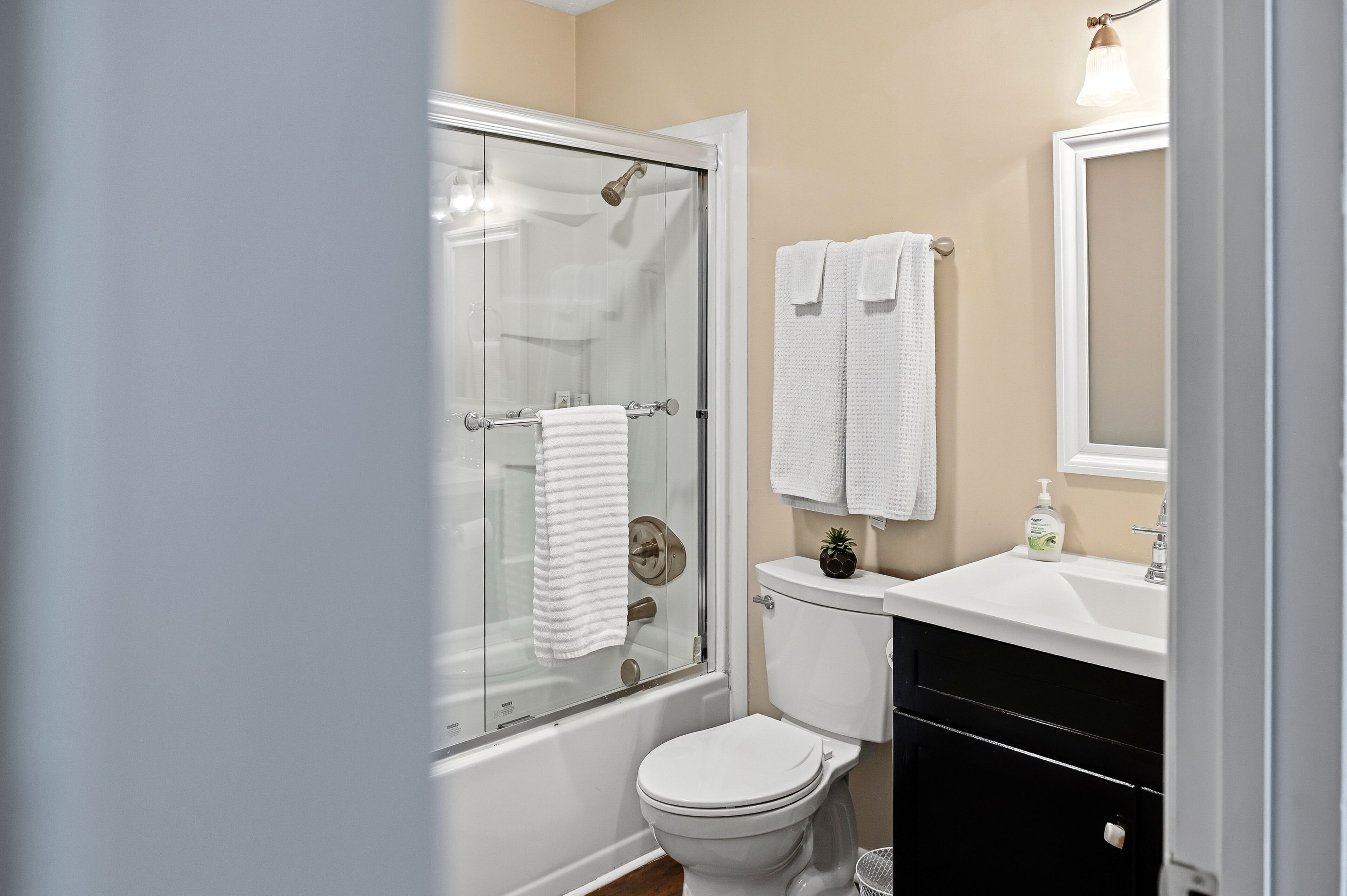 A bathroom with a glass-enclosed shower, a toilet, a sink with a mirror, and two towels hanging on the wall.
