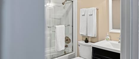 A bathroom with a glass-enclosed shower, a toilet, a sink with a mirror, and two towels hanging on the wall.