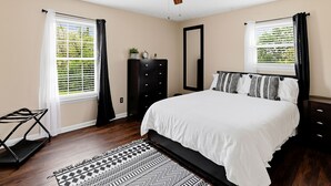 Un dormitorio con cama, cómoda, espejo, ventilador de techo y ventana con persianas.
