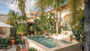 Una piscina rodeada de exuberante vegetación, muros de piedra y mobiliario exterior.