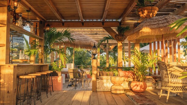 Una terraza de madera con taburetes de bar, sillas de mimbre y plantas en macetas.
