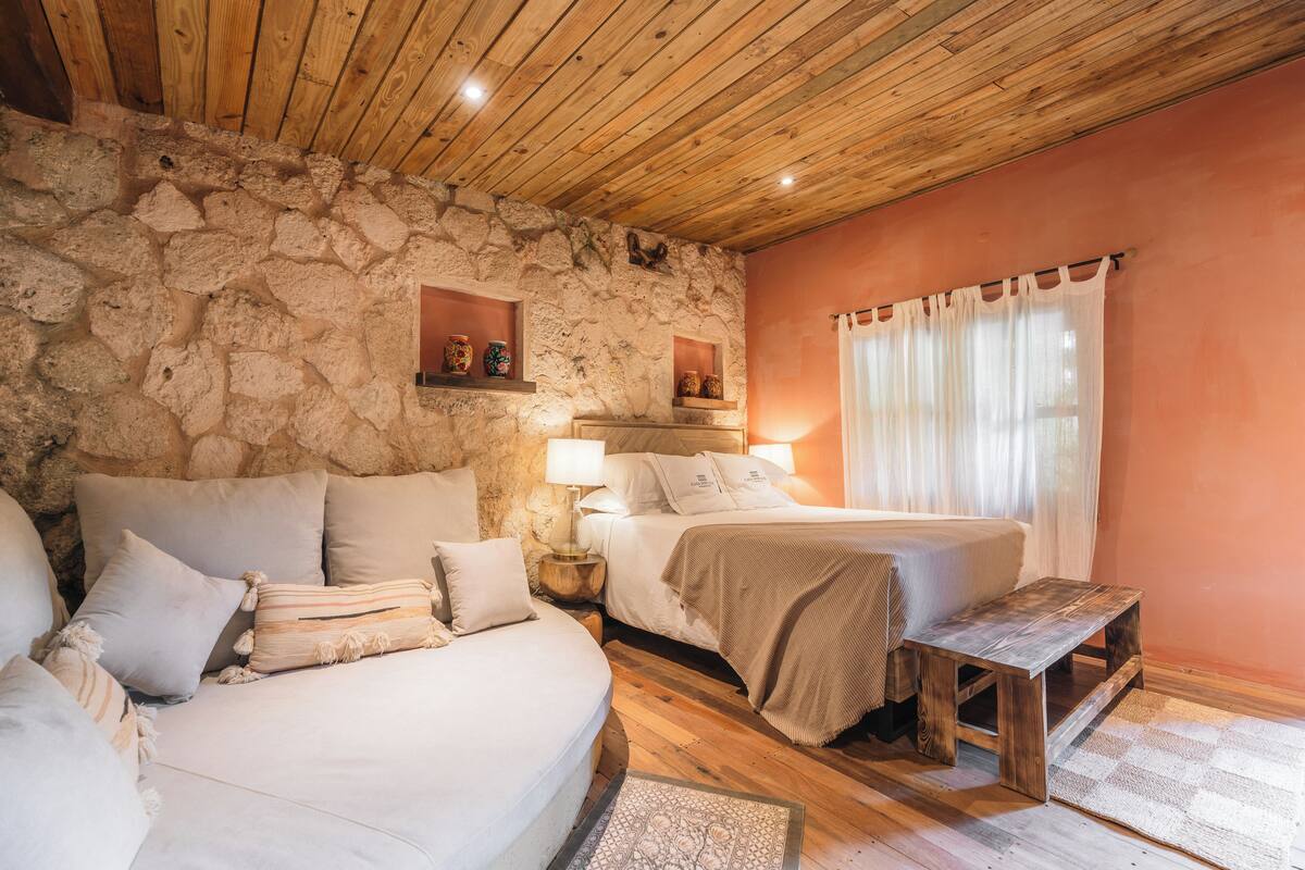 A cozy bedroom with two beds, a stone wall, wooden ceiling, and a small wooden table.