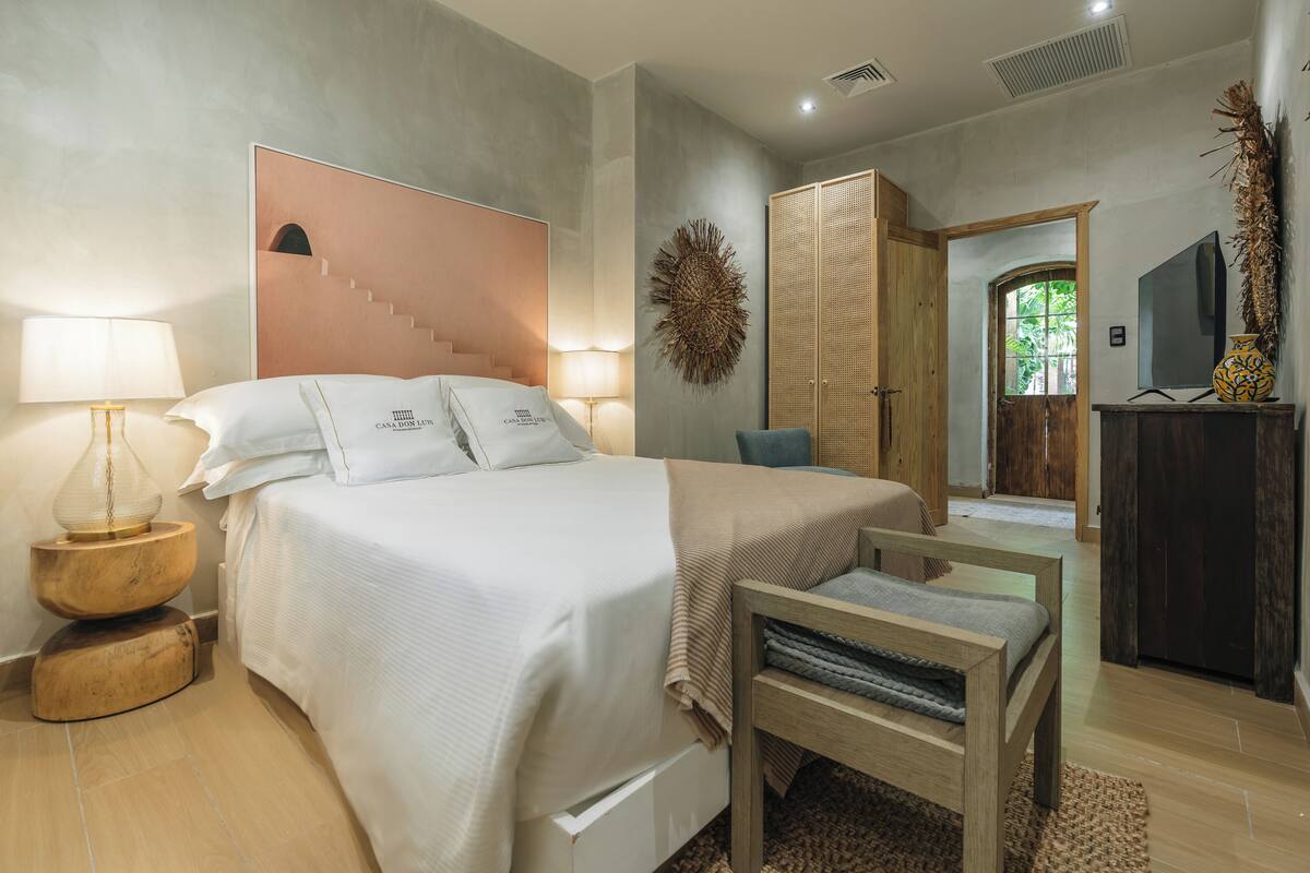 A modern bedroom with a large bed, bedside lamps, a wooden bench, and a wardrobe.