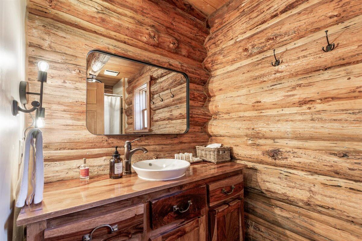 Une salle de bain rustique avec des murs en bois, un grand miroir, un meuble-lavabo en bois et un évier.