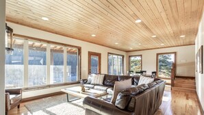 A spacious living room with a wooden ceiling, large windows, a leather sofa, and a coffee table. - Tranquil cabin on Warm River, Ashton
Boat ramp access-fly fishing haven.  (Ashton)