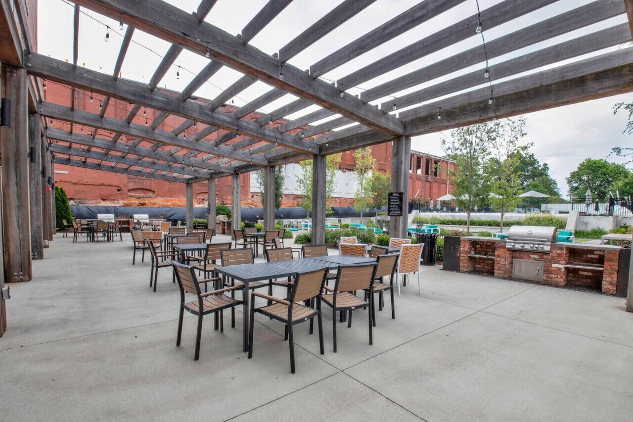 Une terrasse extérieure avec des tables et des chaises, un barbecue et un espace abrité offrant une vue sur un bâtiment en briques.