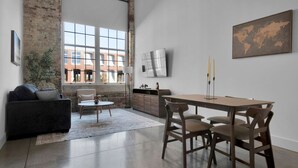 A spacious living room with a large window, a dining area with a wooden table and chairs, a sofa, and a small side table. - Spacious Sanctuary | Near DT Action (Greenville)