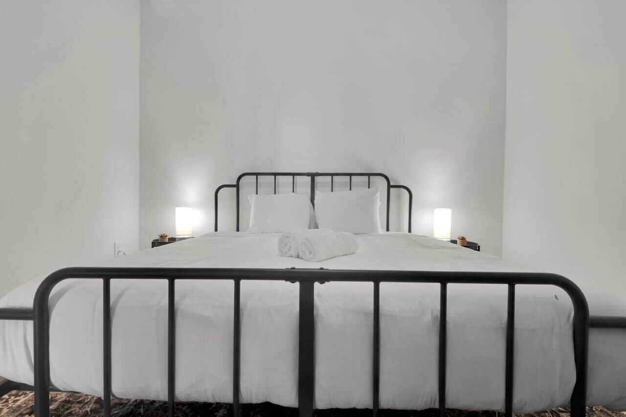 A minimalist bedroom with a metal bed frame, white bedding, and bedside lamps.