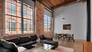 Un salon spacieux avec un grand canapé d’angle, une table basse en verre et un coin repas comprenant des chaises et une table en bois.