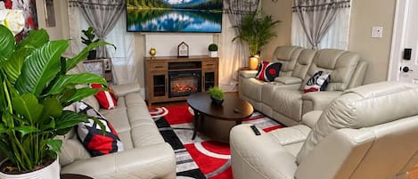 Una sala de estar con chimenea, sofás de cuero, televisor y ventilador de techo.