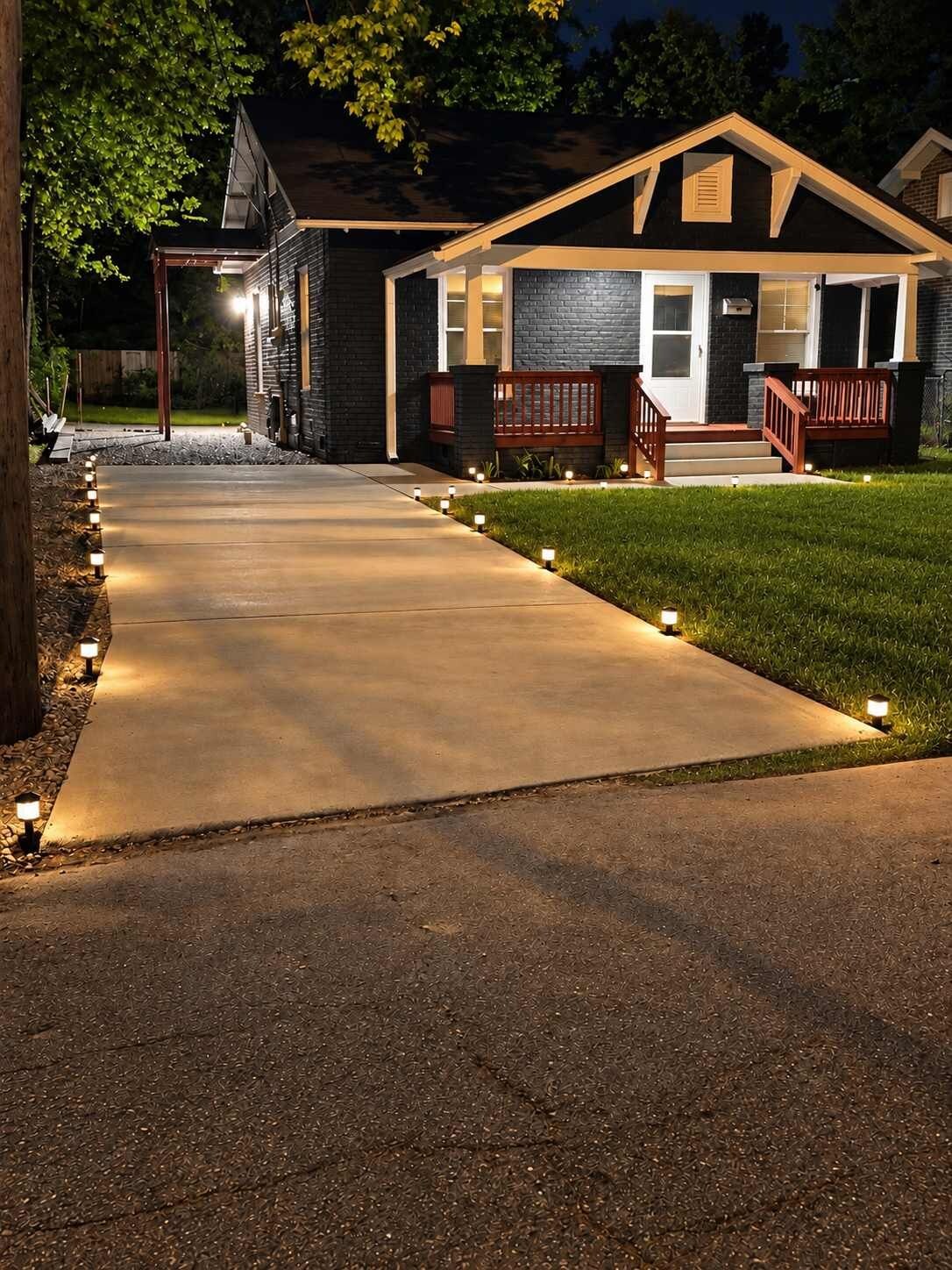 A house with a concrete driveway, a wooden deck, and a well-lit front porch.