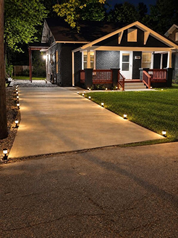 A house with a concrete driveway, a wooden deck, and a well-lit front porch.