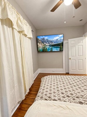A bedroom with a bed, a ceiling fan, a mounted TV, and a door.