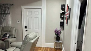 Una sala de estar con un sofá color beige, una mesita auxiliar con un florero y una puerta que da a otra habitación.