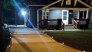 Una casa residencial con un camino de entrada bien iluminado y un porche delantero.
