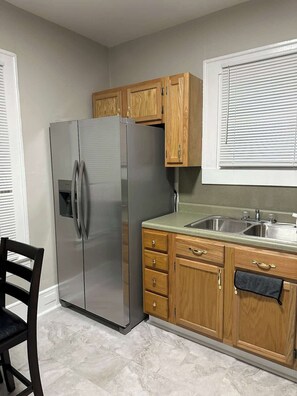 Eine Küche mit Edelstahlkühlschrank, Holzschränken, einer Spüle und einem Stuhl.