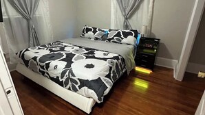 Un dormitorio con cama, cortinas, ventilador de techo y mesita de noche.