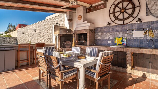 An outdoor dining area with a stone wall, a wooden table, and chairs.