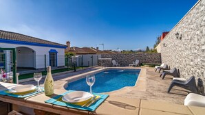 A poolside area with a table set for dining, a pool with a decorative edge, and a stone wall.