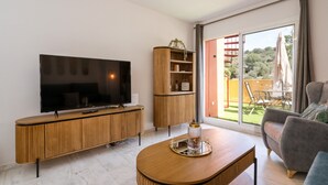 A modern living room with a flat-screen TV, wooden entertainment unit, and a dining table with a glass candle holder. - Marbella Coastal Comfort (Marbella)