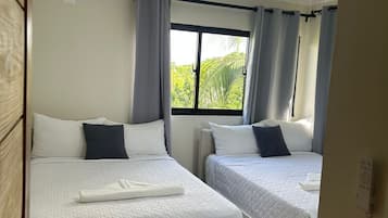 Habitación de hotel con dos camas, una ventana con cortinas, ventilador de techo y vista a zonas verdes.