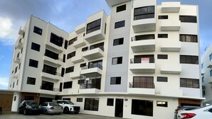 Un immeuble résidentiel à plusieurs étages, doté de balcons, d’un espace de stationnement et d’un panneau indiquant les logements disponibles.