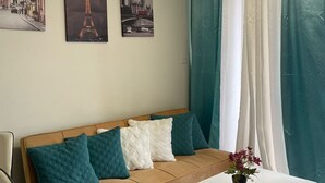 Una sala de estar moderna con un sofá color beige, cojines verde azulado, una mesa de centro blanca y dos cuadros enmarcados con imágenes de monumentos famosos.