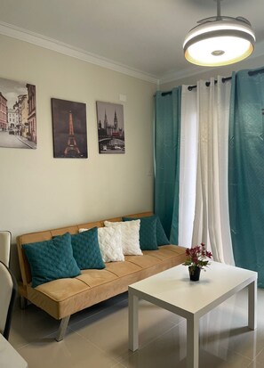 A modern living room with a beige sofa, teal cushions, a white coffee table, and two framed pictures of famous landmarks. - FREE CLEANING / NO FEES / Comfortable Apartment Near AILA Airport and Boca Chica (Santo Domingo Este)